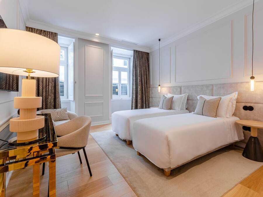 Habitación de hotel con dos camas, un escritorio con lámpara, una silla y una mesita.