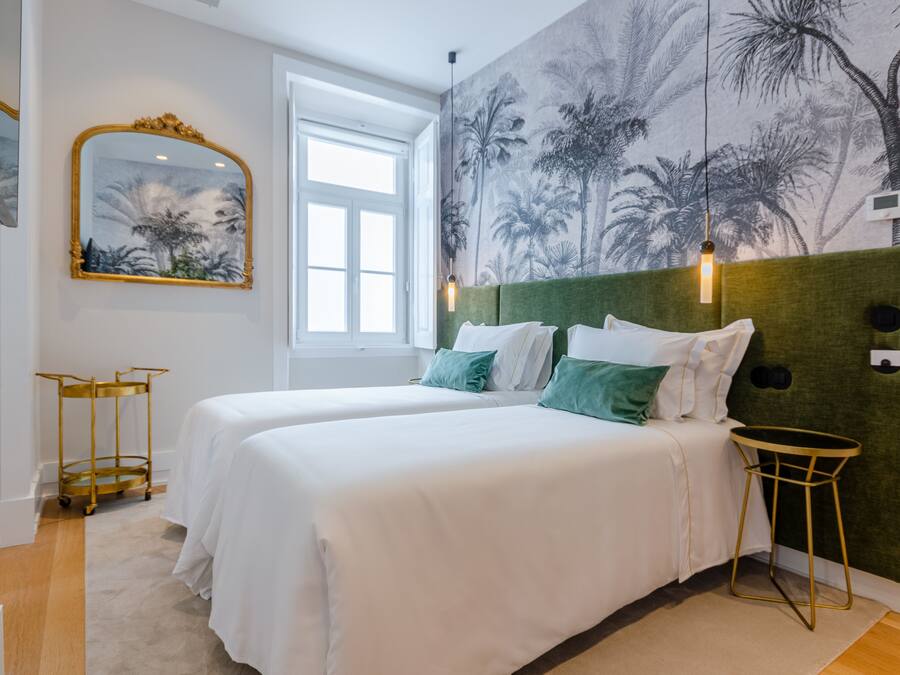 Habitación de hotel con dos camas, cabecera verde, un espejo grande, un mural en la pared y una mesita de noche pequeña.