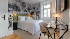 A bedroom with a bed, a glass table, a chair, a lamp, and a wall with a palm tree mural. - BCascais Boutique House by APT IIN - Cascais Center (Cascais)
