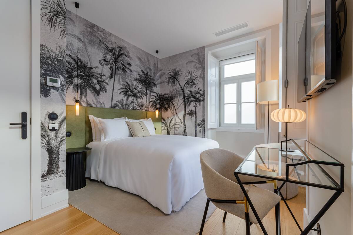 Une chambre à coucher comprenant un lit, une table en verre, une chaise, une lampe et un mur orné d’une fresque représentant un palmier.