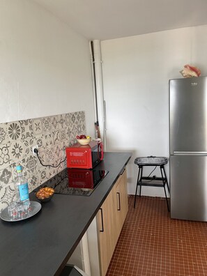 Una cocina con encimera negra, microondas rojo, refrigerador de acero inoxidable y salpicadero con estampado.