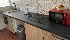 A kitchen with a sink, a microwave, a bowl of fruit, and a trash bin. - Maison Bel bonjou (Le Marin)
