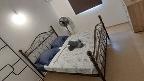 A bedroom with a bed, a fan, a window, and a small wooden cabinet. - Maison Bel bonjou (Le Marin)