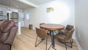 Una cucina moderna con mobili bianchi, un frigorifero in acciaio inossidabile e un'area pranzo con un tavolo rotondo e quattro sedie.