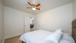 Una camera da letto con un letto, una ventola a soffitto e una porta che dà su un'altra stanza.