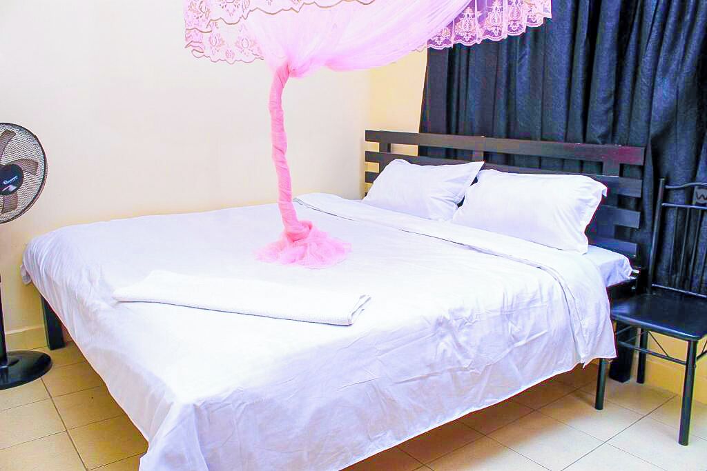 Un lit recouvert d’une couverture blanche, surmonté d’un dais rose et agrémenté d’une chaise noire.