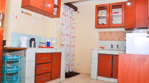 A compact kitchen with wooden cabinets, a coffee maker, and a refrigerator. - MILANY HOMES - NEAR JKIA AIRPORT (Syokimau)