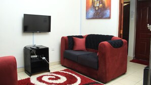 A living room with a red sofa, a black entertainment unit, and a flat-screen TV mounted on the wall. - MILANY HOMES - NEAR JKIA AIRPORT (Syokimau)