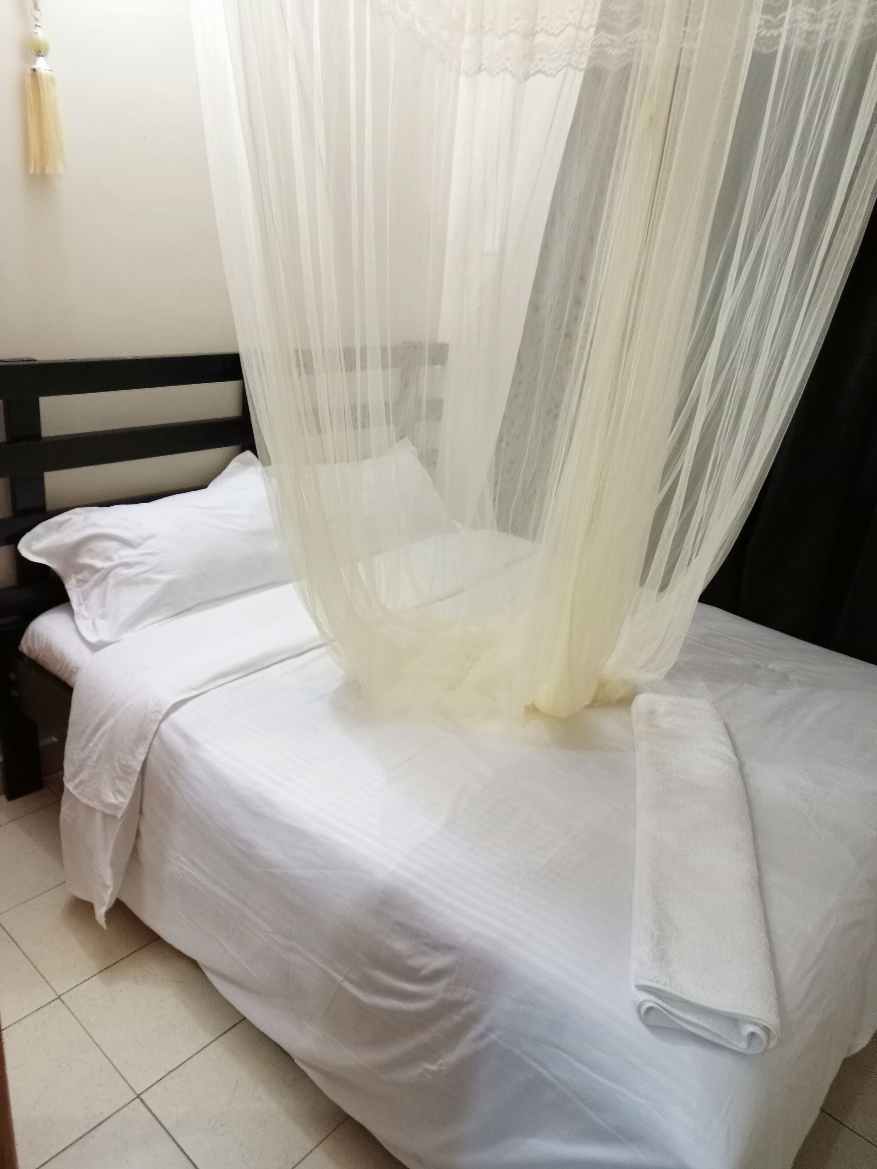 A bed with a white bedspread and a white pillow, a black headboard, and a white canopy.