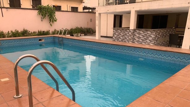 Una piscina rectangular con borde de azulejos y barandillas de metal.