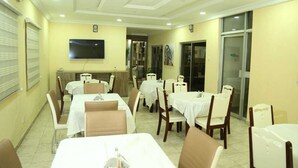 Un comedor con mesas y sillas, un televisor de pantalla plana montado en la pared y una puerta que da a otra habitación.