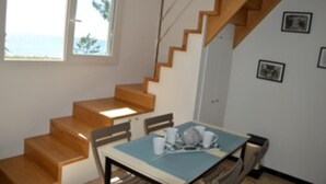 Ein Zimmer mit einer Holztreppe, einem Esstisch mit Stühlen und einem Fenster mit Meerblick.
