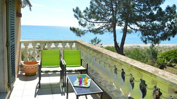 Ein Balkon mit zwei grünen Stühlen, einem Tisch mit einer Auswahl an bunten Gläsern und Blick aufs Meer.