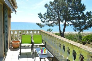 A balcony with two green chairs, a table with a tray of colorful glasses, and a view of the sea. - A Balcony on the Mediterranean 2 (Taglio-Isolaccio)