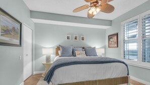 A bedroom with a bed, a ceiling fan, a window with blinds, and wall art.