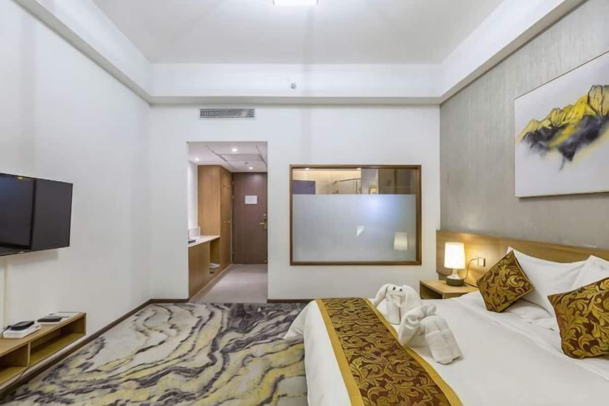 A hotel room with a bed, a TV, a desk, and a mirror.