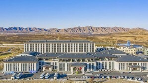 A hotel with a modern architectural design, a parking lot, and a mountainous backdrop. - Dahua Jianguo Hotel (Zhuolu)