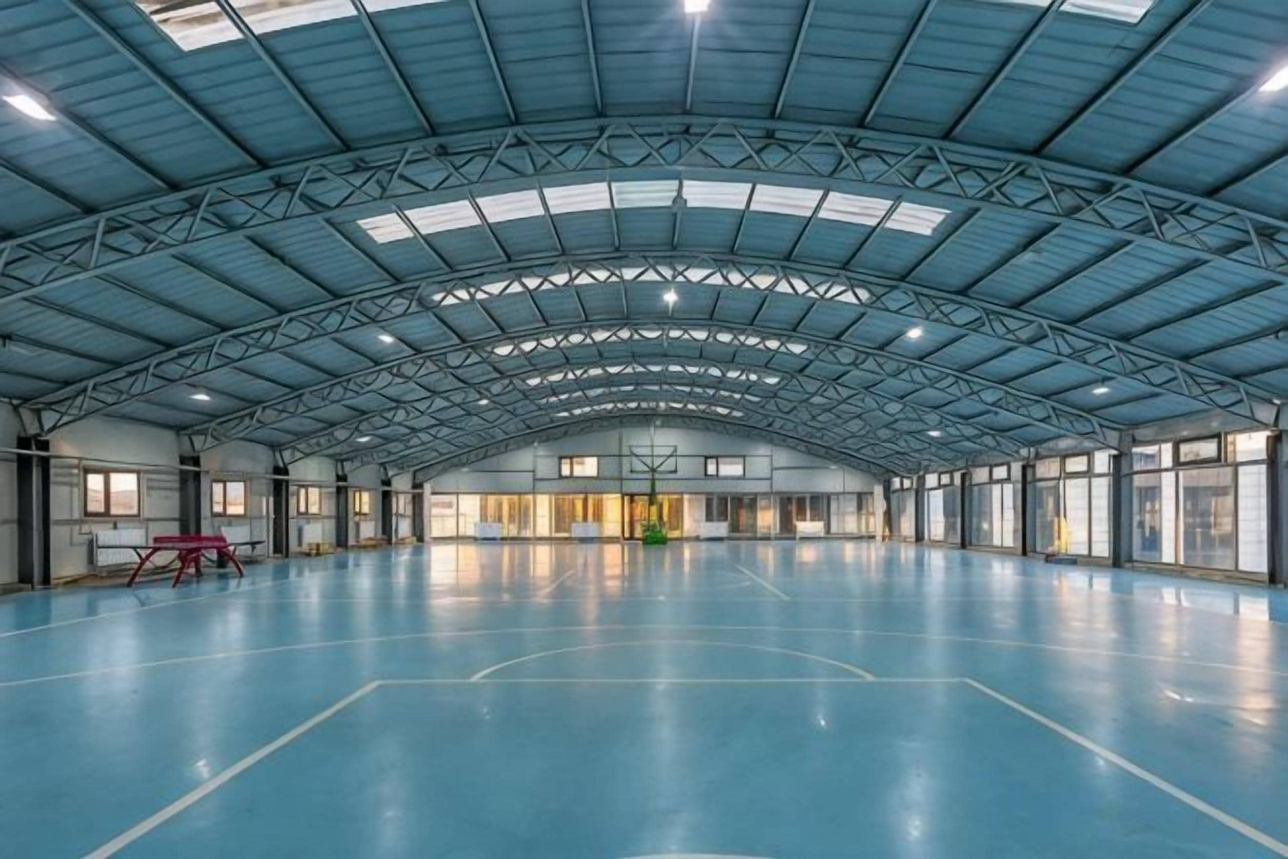 An indoor sports hall with a high ceiling, a basketball court, and a visible basketball hoop.