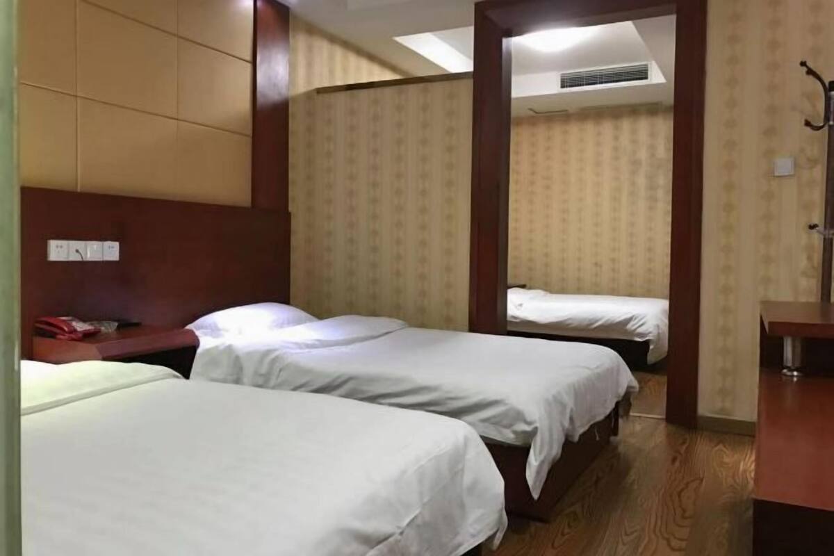 A hotel room with two single beds, a wooden floor, a small desk, and a mirror.