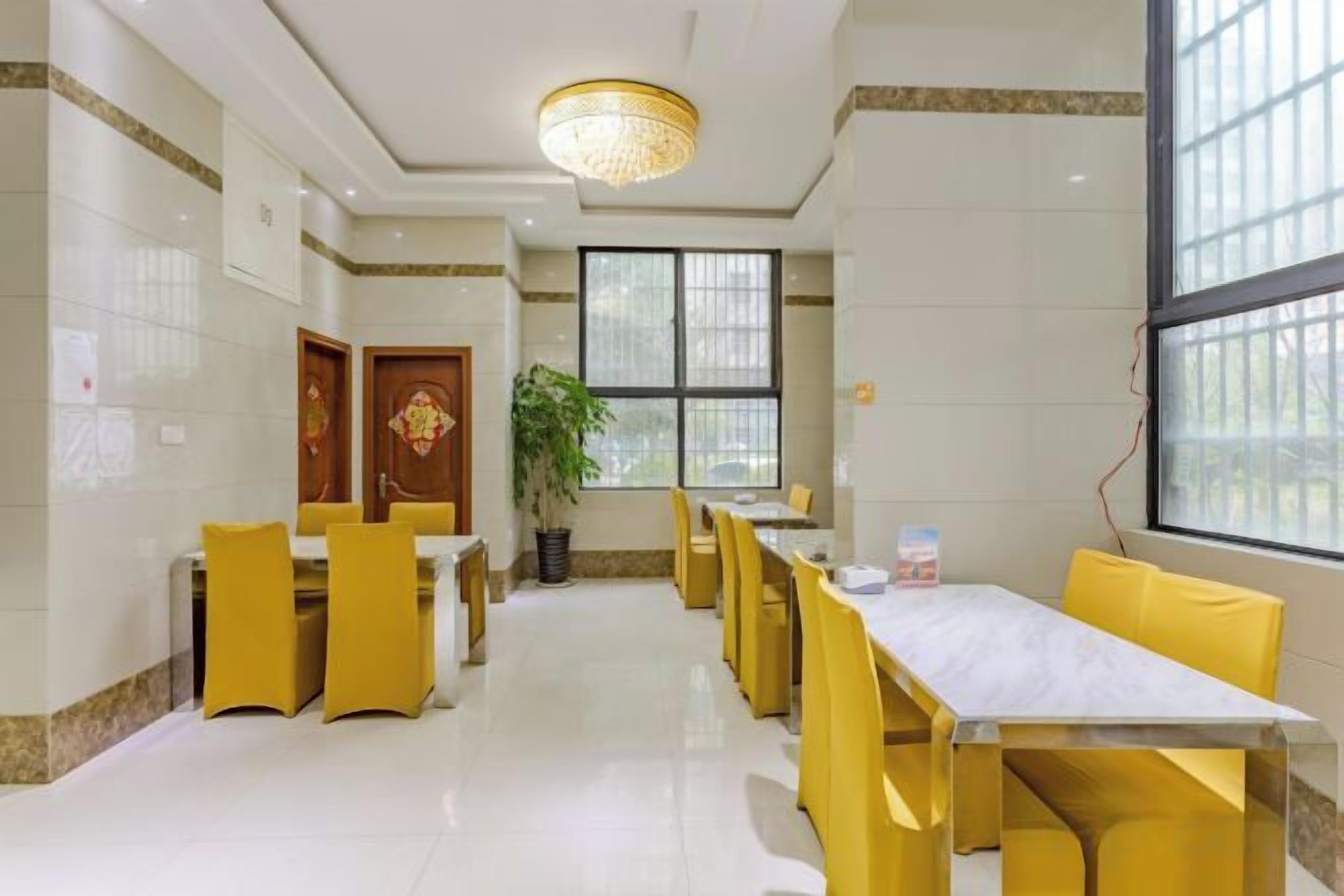 A hotel dining area with yellow chairs and tables, a chandelier, and large windows.