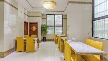 A hotel dining area with yellow chairs and tables, a chandelier, and large windows.