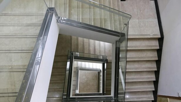 Un escalier moderne avec des rampes en verre et des carreaux de couleur beige.