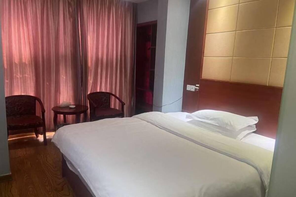 A hotel room with a bed, two chairs, a small table, and a curtain.