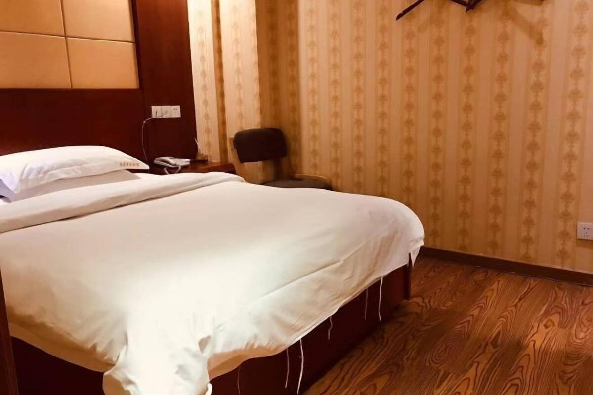 A hotel room with a bed, a chair, a wall-mounted telephone, and a patterned wallpaper.