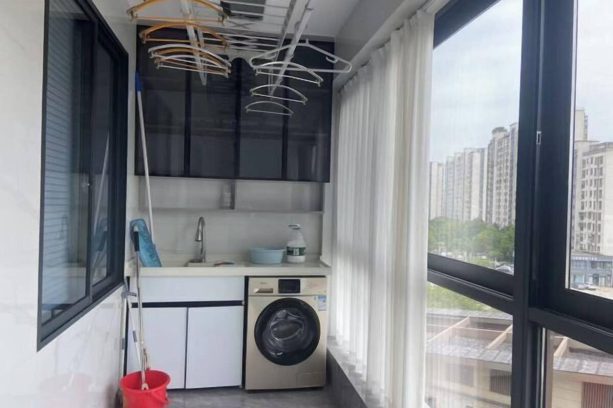 A compact laundry room with a washing machine, a drying rack, and a mop.