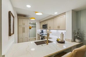 A modern kitchen with white marble countertops, gold handles, and a central island with a sink and faucet.
