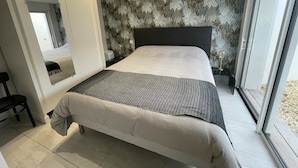 A bedroom with a bed, a mirror, a nightstand, and a window.