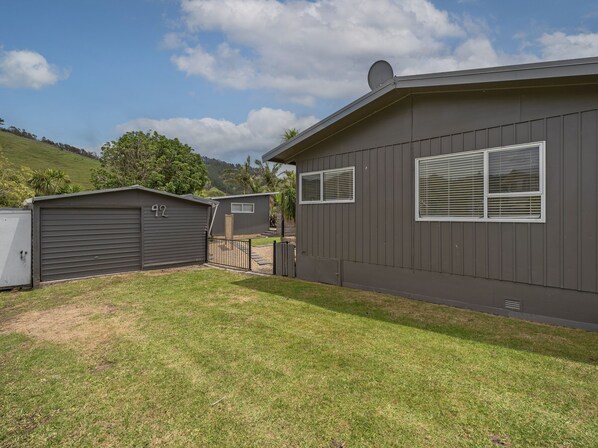 A residential property with a garage, a covered patio, and a house with a satellite dish. - Kon Tiki Retreat - Whiritoa Beach Holiday Home (Whiritoa)