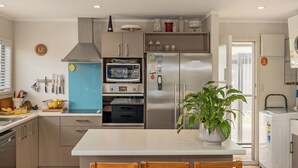 A modern kitchen with a central island, stainless steel appliances, and a potted plant. - Kon Tiki Retreat - Whiritoa Beach Holiday Home (Whiritoa)