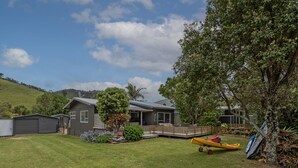 A residential property with a covered patio, a fenced yard, and a canoe. - Kon Tiki Retreat - Whiritoa Beach Holiday Home (Whiritoa)