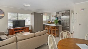 A modern kitchen with a microwave, refrigerator, and a dining area with a wooden table and chairs. - Kon Tiki Retreat - Whiritoa Beach Holiday Home (Whiritoa)