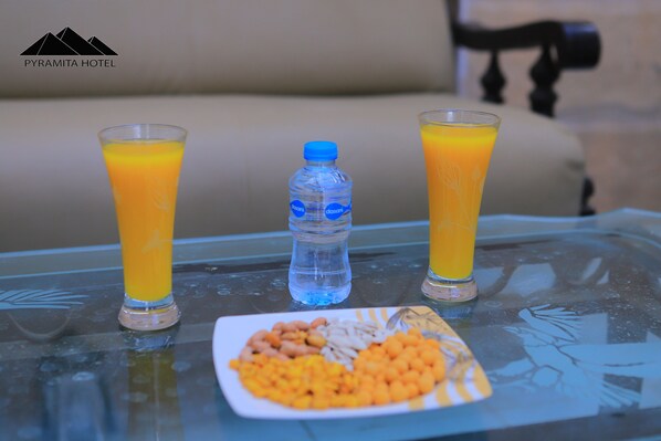 A glass table with two glasses of orange juice, a bottle of water, and a plate of cereal.