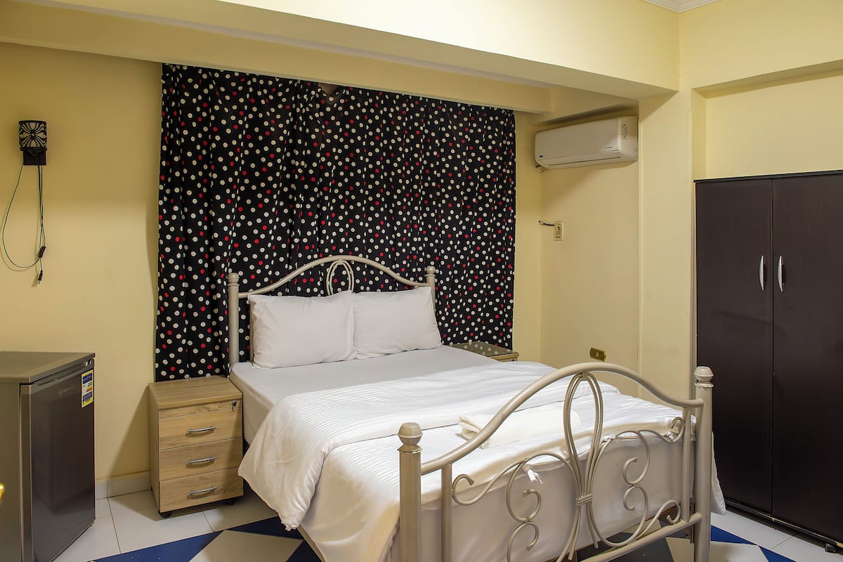A neatly arranged bedroom with a bed, bedside table, wardrobe, and a small desk with a chair.