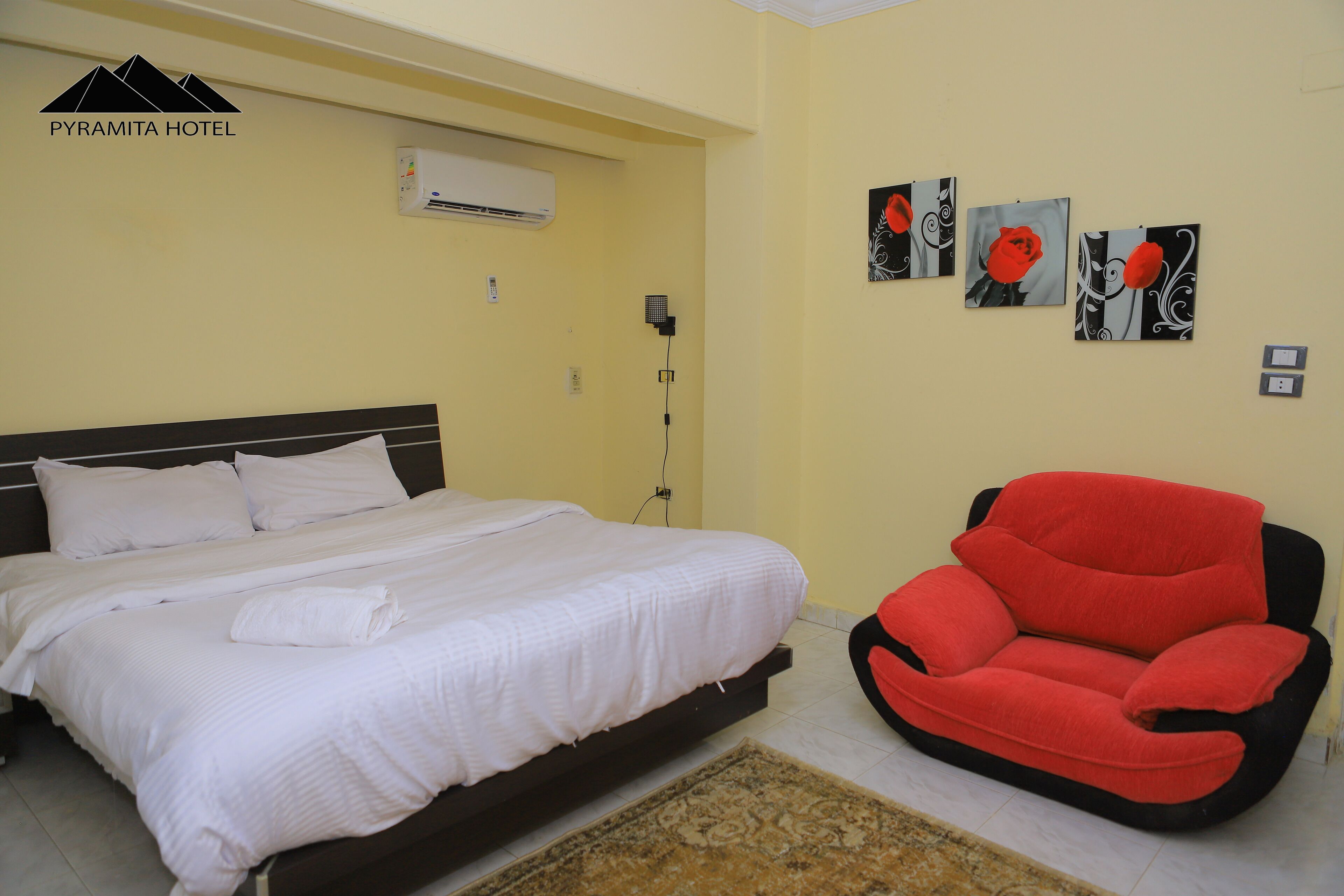 Habitación de hotel con una cama, una silla roja y tres obras de arte colgadas en la pared.
