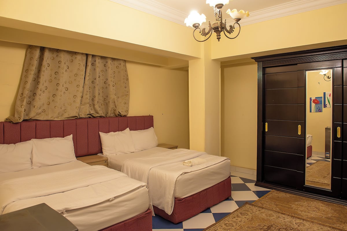 A hotel room with two beds, a checkered floor, a large mirror, and a chandelier.