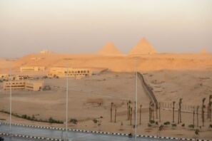 A desert landscape with pyramids in the background and a road in the foreground. -  Pyramita Hotel (Giza)