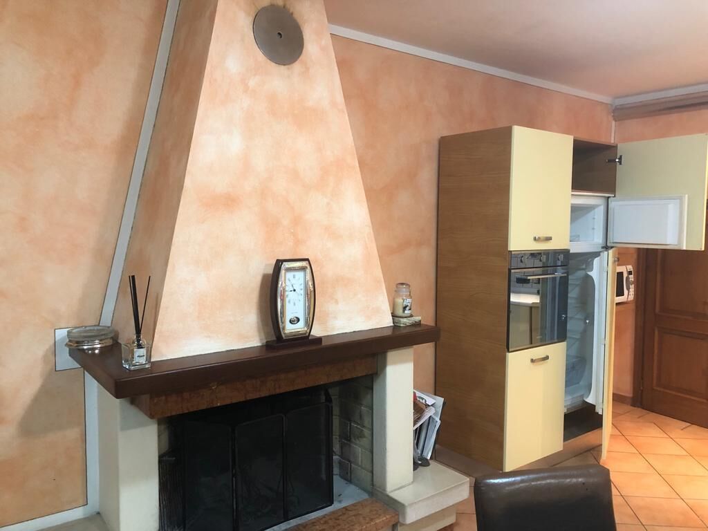 A living room with a fireplace, a clock, and a kitchen area with cabinets and appliances.