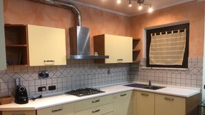 A kitchen with light-colored cabinets, a gas stove, a sink, and a window with a curtain. - Cozy and independent apartment with garden! (Borgo A Buggiano)