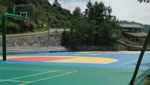 An outdoor basketball court with two hoops, a stone wall, and a building in the background. - Cliff Hotel (Luocheng)