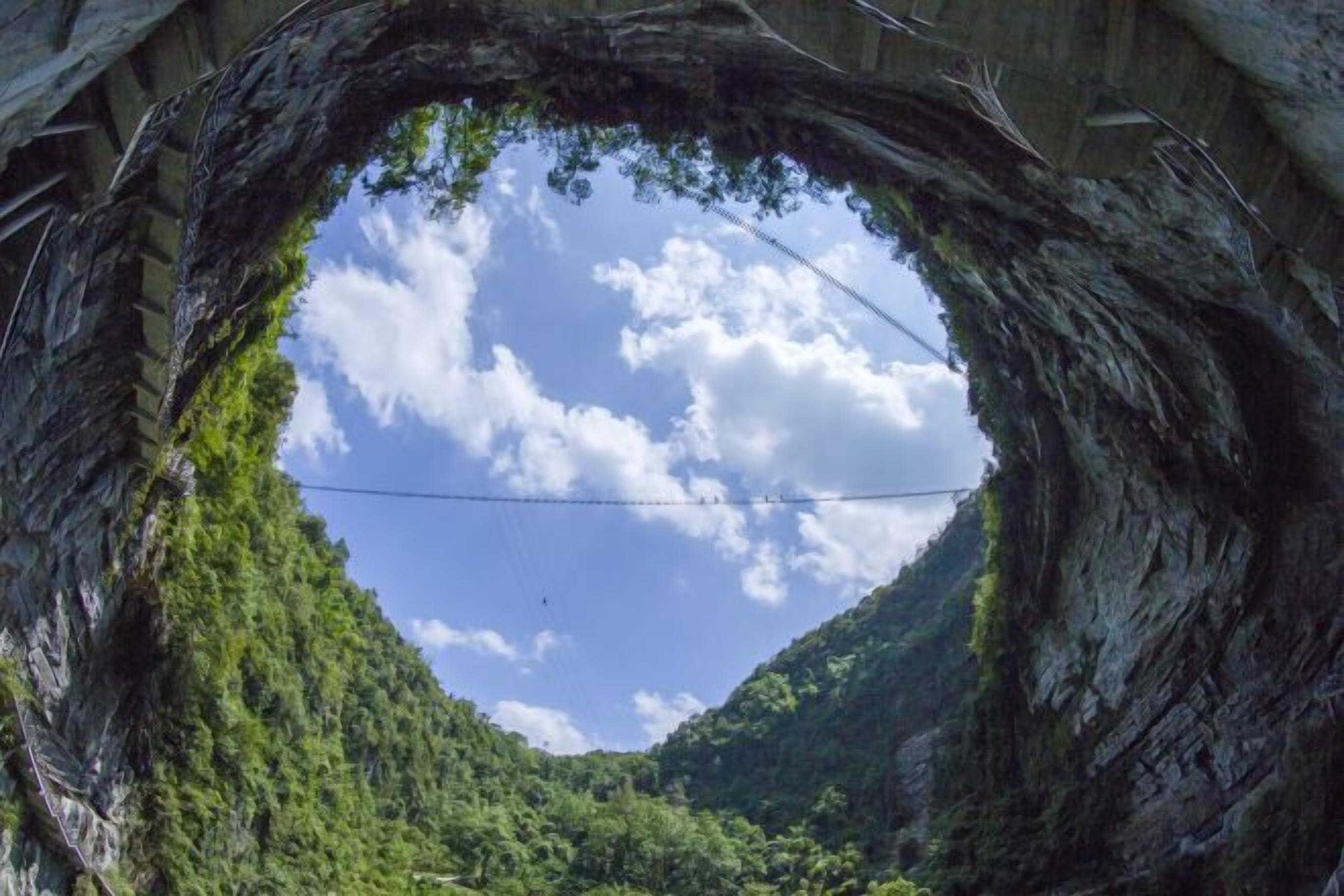 A heart-shaped tunnel with a clear sky and greenery inside.