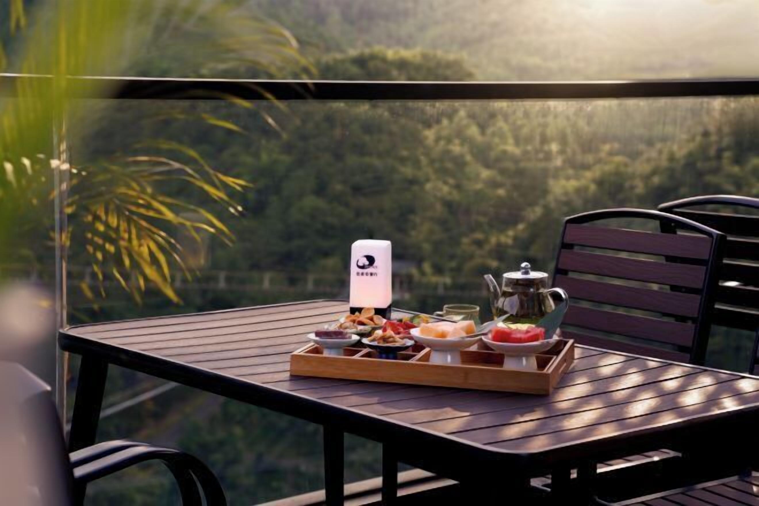 Una mesa con una bandeja de comida y una tetera en un balcón con vistas a una zona boscosa.