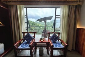 Una habitación con una mesa y dos sillas, una ventana con cortinas y vistas a un paisaje montañoso.