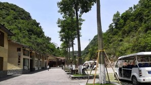 A pathway lined with trees and a row of traditional-style buildings with a clear sky above. - Cliff Hotel (Luocheng)