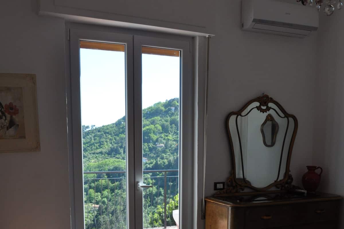 A bedroom with a bed, a dresser, a mirror, and a balcony with a view of greenery.