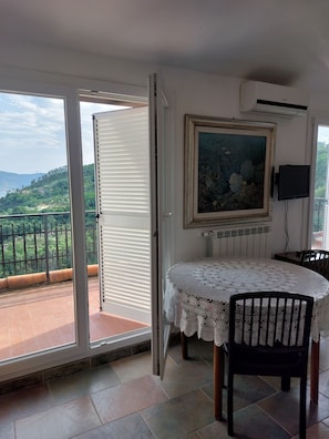 A balcony with a view of a green landscape, a table with a lace tablecloth, and a painting on the wall. - Oliva Azzurra (Vezzano Ligure)
