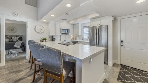 A modern kitchen with white cabinetry, stainless steel appliances, and a central island with bar stools.